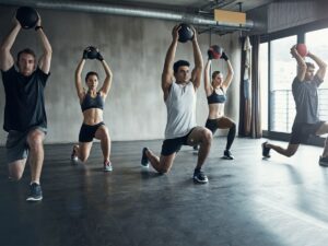 Fitness group performing lunges with medicine balls in a studio with concrete walls.