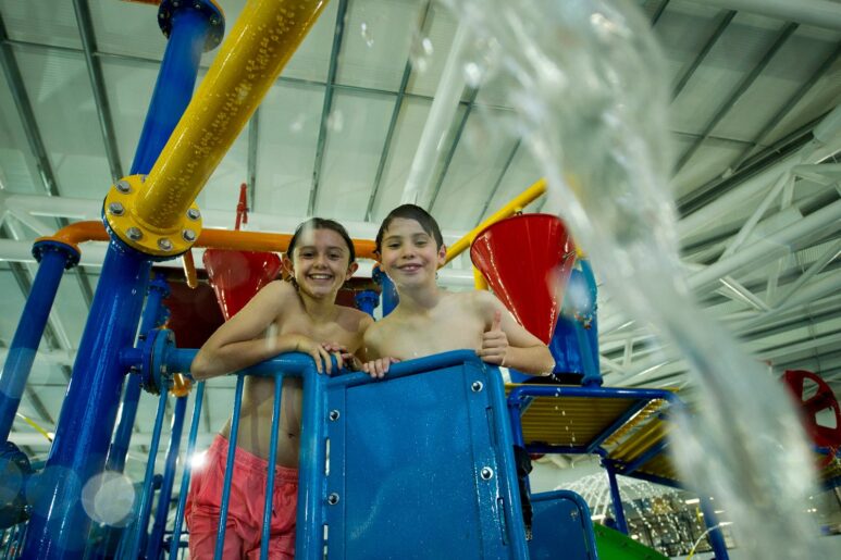 Children enjoying AquaPulse Hoppers Crossing indoor water play zone, smiling from the top of the colourful splash structure.