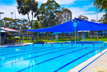 Bright blue 8‑lane outdoor lap pool at WynActive’s Werribee Outdoor Pool, featuring expansive shade sails over the water, framed by leafy trees and landscaped lawns—perfect for lap swimming, fitness, and family recreation. swimming carnivals WynActive