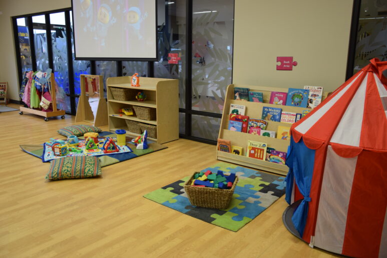 Indoor play area featuring a reading nook, circus-themed play tent, baskets of toys, and soft floor mats.