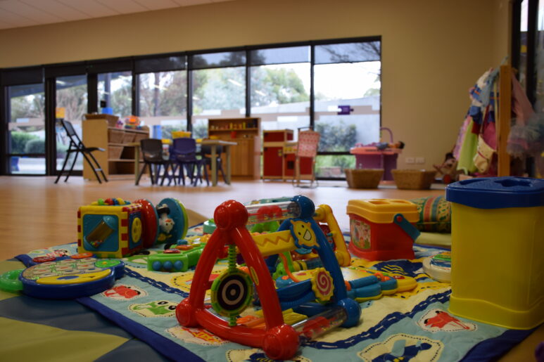 Colourful play mat with baby toys and activity centres inside a bright childcare room.