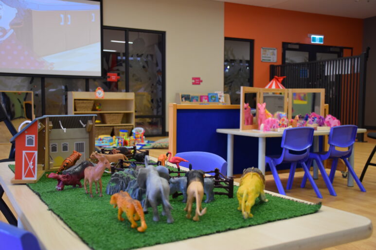 Close-up of a toy farm set with animal figurines on a play table, with other activity areas in the background.