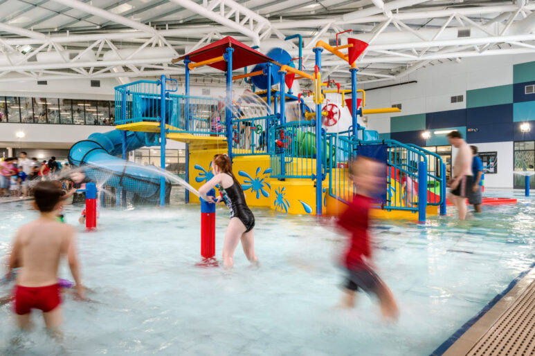 Children playing in the AquaPulse Hoppers Crossing indoor water play area with slides, splash buckets, and fountains.