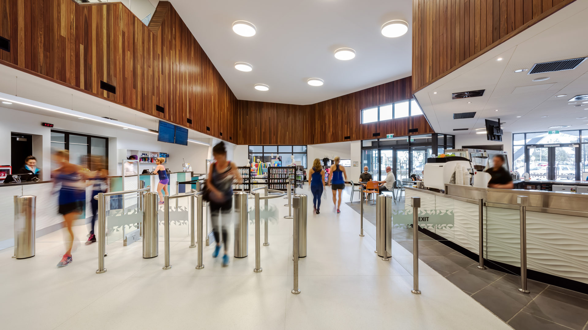 AquaPulse Hoppers Crossing reception area with timber panelling, café seating, and visitors entering through turnstiles.