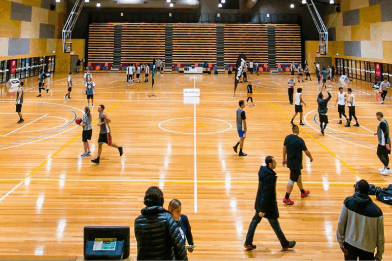 Junior netball teams warming up and practicing on the polished indoor courts at Eagle Stadium, with coaches and spectators nearby.