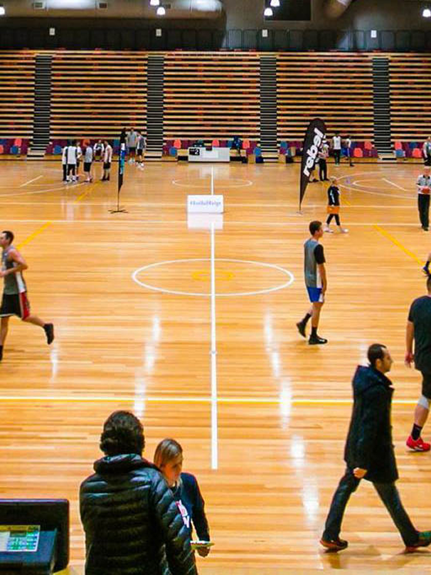 Indoor basketball courts at Eagle Stadium in Werribee with players practising and people walking across the polished timber flooring.
