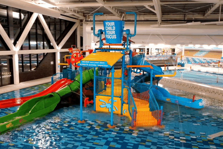 Indoor water play structure at AquaPulse Hoppers Crossing featuring colourful slides, tipping buckets, and splash features.
