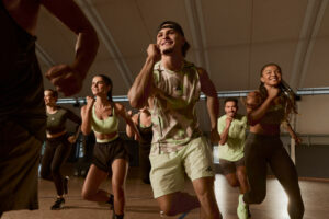 Energetic group workout class with participants running in place and smiling in a brightly lit studio.
