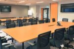 Modern meeting room at Eagle Stadium with long conference tables, black chairs, wall-mounted screens, and bright orange accents.