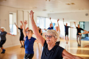 Seniors participating in an energetic group fitness class at WynActive, raising arms and moving with enthusiasm.