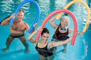 Three adults in a pool holding colourful foam noodles for resistance training during an aqua fitness session.