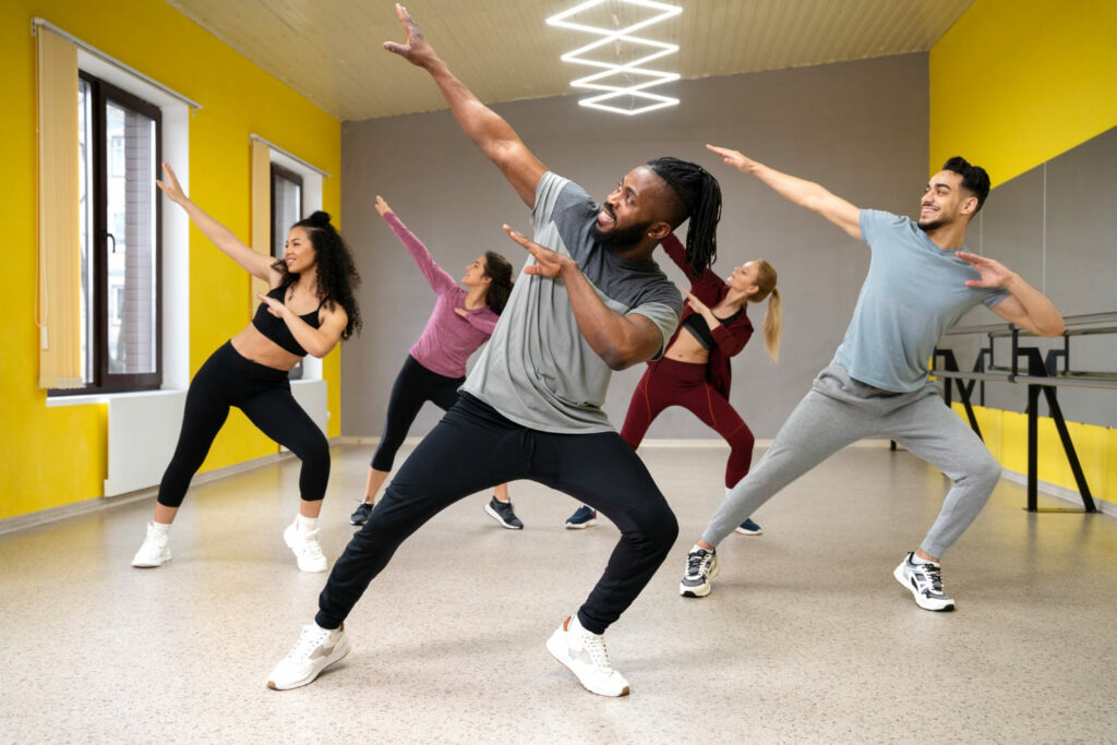 Group of people enjoying a dance fitness class, following an instructor in a bright studio with yellow walls.