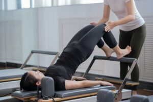 Woman using a Pilates reformer machine with guidance from an instructor.